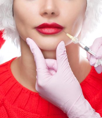 The doctor cosmetologist makes injection on the lips of a woman in the Santa Claus hat.